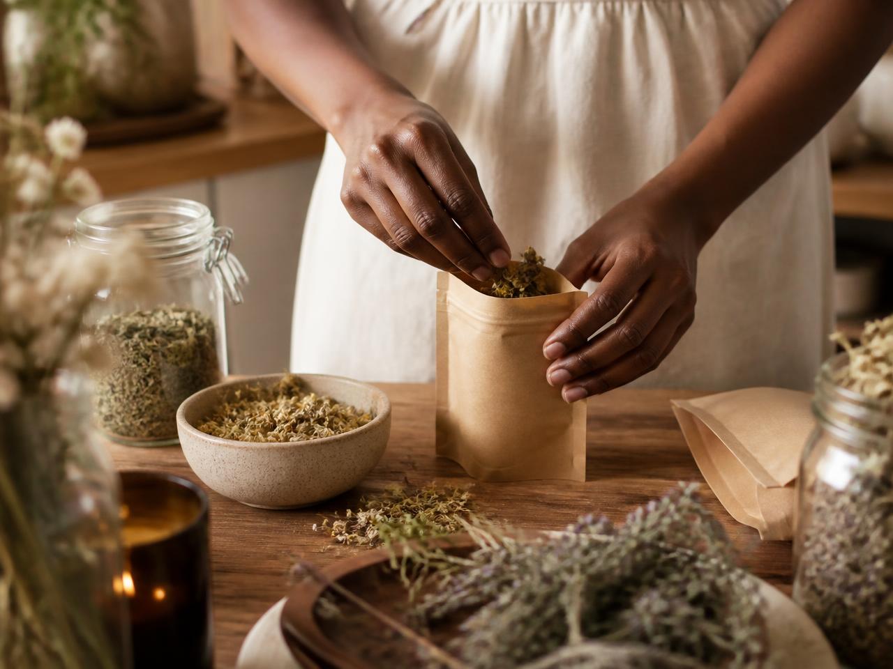 Hands packing dried herbs into a kraft pouch
